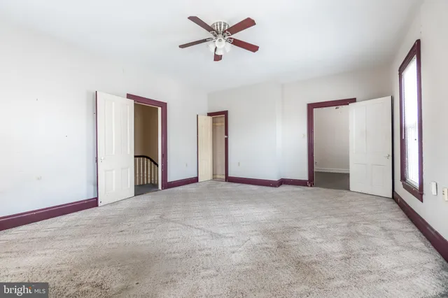 an empty room with chandelier fan and windows