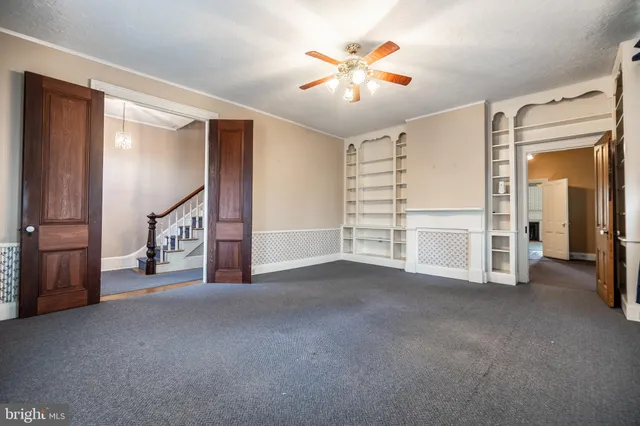 an empty room with chandelier fan and windows