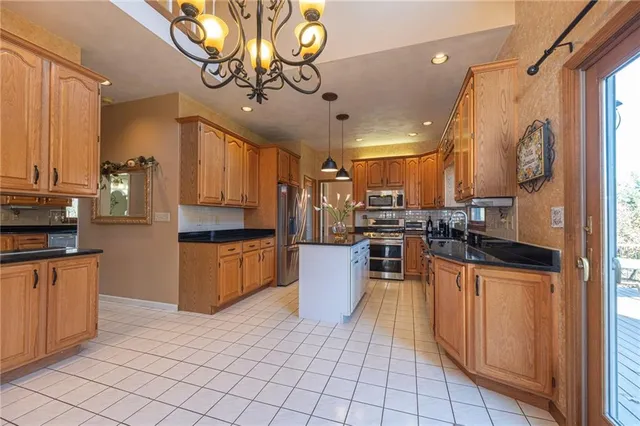 a kitchen with stainless steel appliances kitchen island granite countertop a refrigerator a stove top oven and a sink with granite countertops