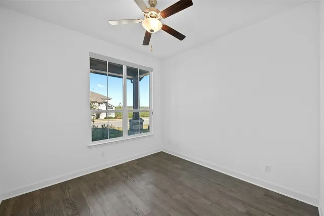 an empty room with wooden floor chandelier fan and windows