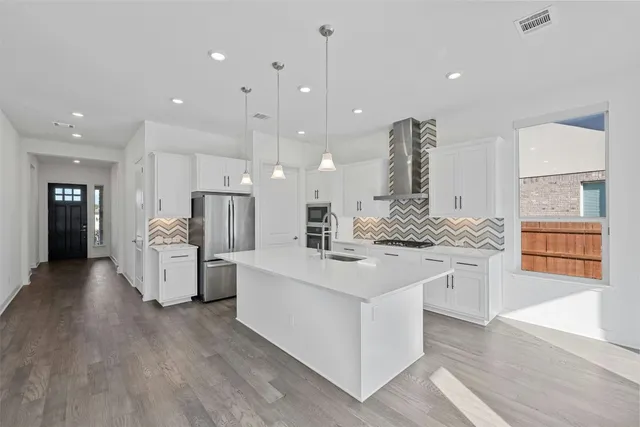 a large white kitchen with stainless steel appliances kitchen island a stove a refrigerator a oven and a dining table with wooden floor