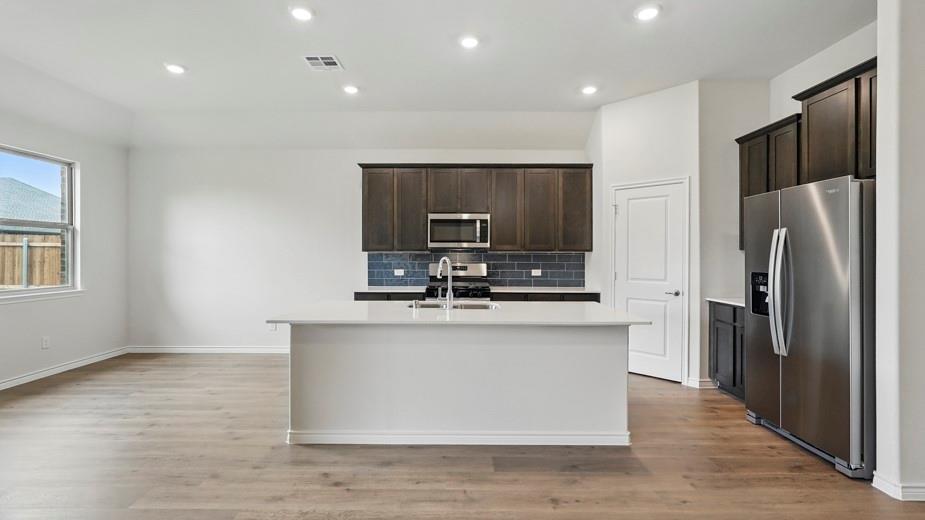 4162 Waldron Trail Forney, TX 75126 - Photo 6 of 29 Contemporary kitchen featuring an expansive island with a stainless steel sink and faucet, dark wood-finish cabinetry, stainless steel appliances, and a tiled backsplash