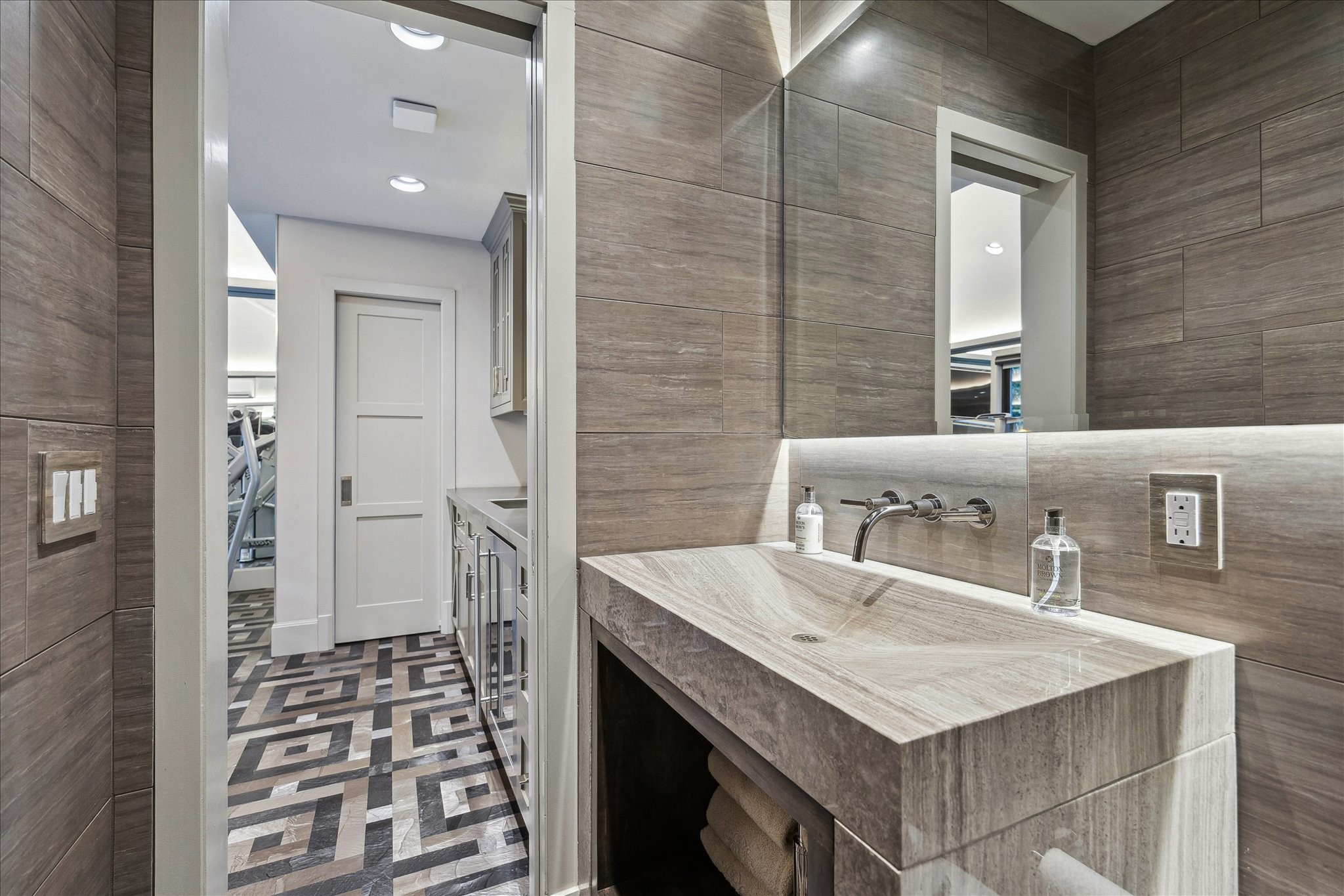 220 Merrie Way Lane Houston, TX 77024 - Photo 45 of 50 Located in the detached fitness space, this modern powder bath features a backlit onyx countertop with an integrated sink, paired with a designer backlit mirror and polished nickel wall-mounted faucet. Neutral tile walls, recessed LED lighting, and a sleek TOTO wall-hung commode complete the bathroom.
