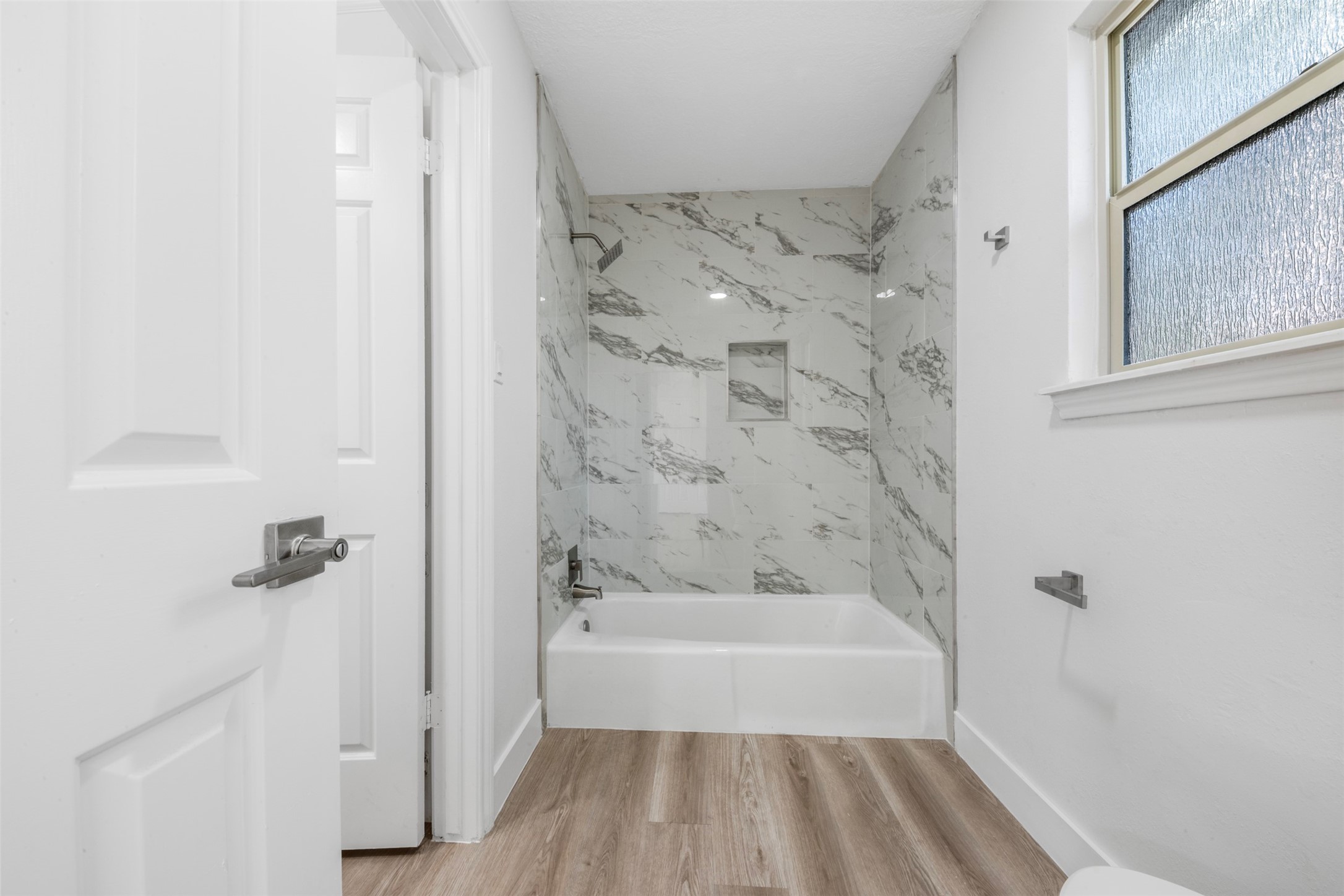 9543 Enstone Circle Spring, TX 77379 - Photo 29 of 50 This bathroom features a modern design with a marble-tiled shower and bathtub, complemented by light wood flooring and a frosted window for privacy.