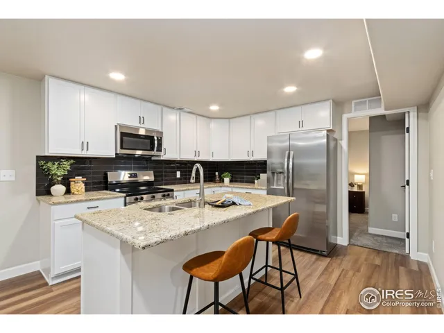 a kitchen with stainless steel appliances granite countertop a refrigerator a stove a sink dishwasher and white cabinets with wooden floor