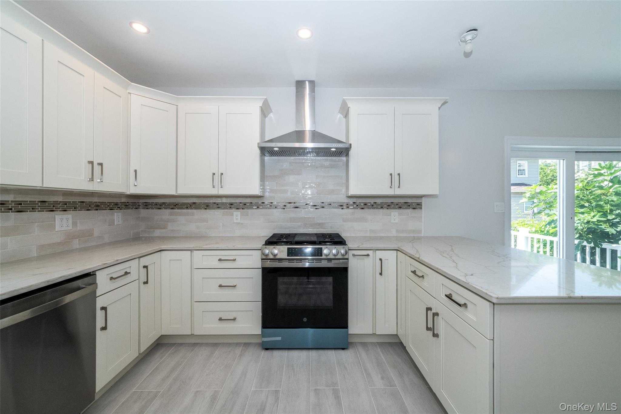 7 Alpha Place, Unit FIRST New Rochelle, NY 10805 - Photo 9 of 25 Kitchen featuring appliances with stainless steel finishes, wall chimney exhaust hood, a peninsula, white cabinets, and light stone countertops