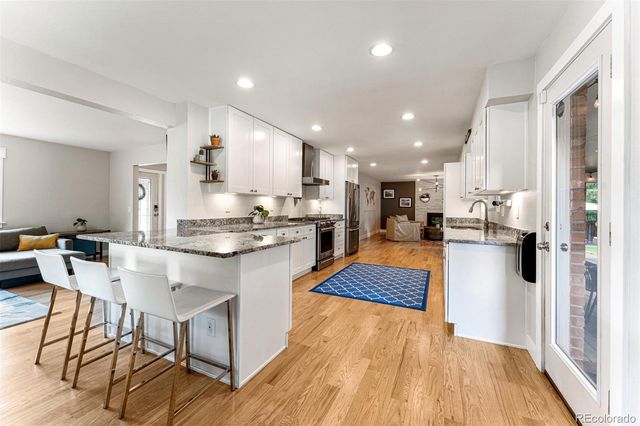 a kitchen with stainless steel appliances granite countertop a refrigerator oven a sink dishwasher and a dining table with wooden floor