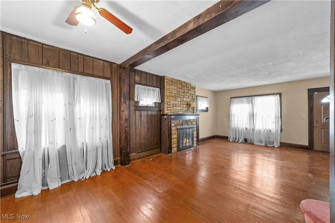15908 Hazel Road Cleveland, OH 44112 - Photo 6 of 20 Unfurnished living room with beam ceiling, wood-type flooring, wooden walls, a fireplace, and a ceiling fan