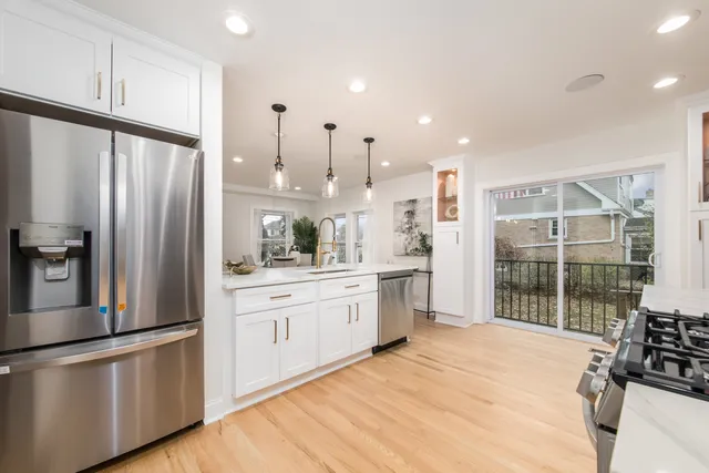 a large kitchen with stainless steel appliances a refrigerator a sink a stove and white cabinets with wooden floor