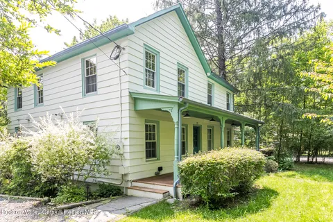 a view of a white house next to a yard with plants and trees