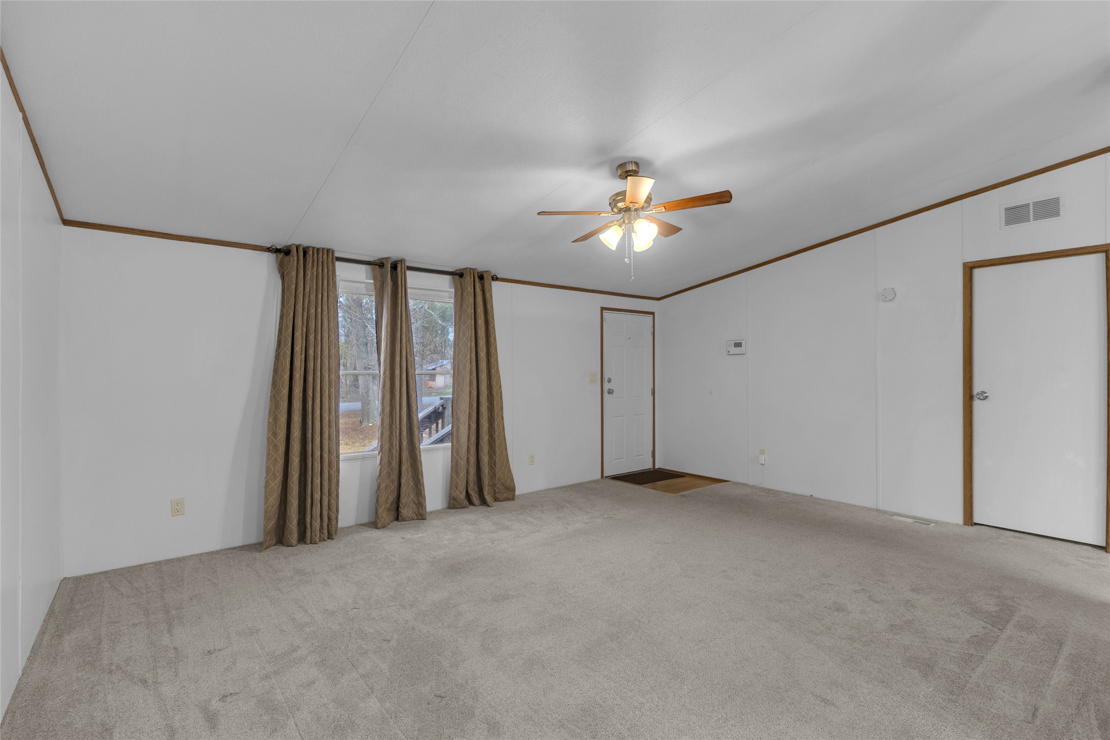 22094 Spear Road Porter, TX 77365 - Photo 19 of 45 This room features neutral carpeting, white walls with wooden trim, a ceiling fan with lights, and large windows with curtains. It has both an entry door and an interior door, offering good natural light.