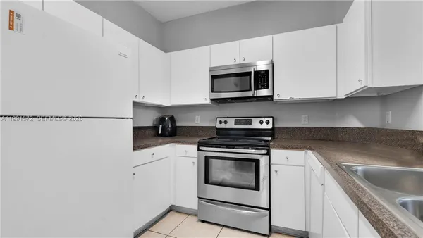 a kitchen with stainless steel appliances granite countertop white cabinets a sink a stove a microwave and a refrigerator