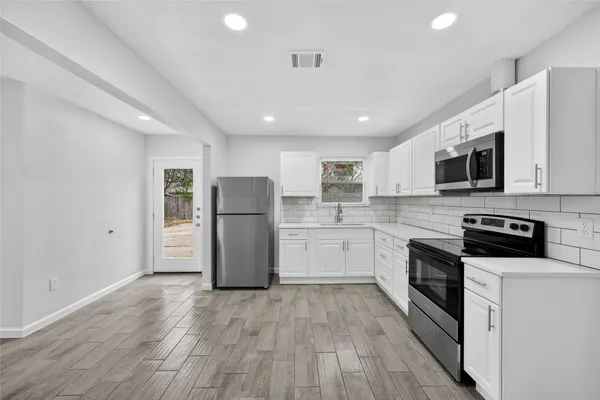 a kitchen with stainless steel appliances granite countertop a refrigerator a stove top oven a sink and cabinets with wooden floor