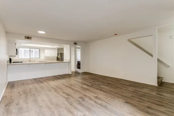 a view of an empty room with kitchen and window