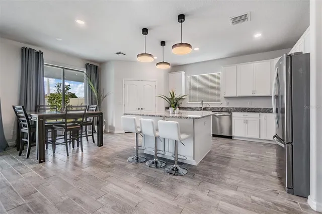 a kitchen with stainless steel appliances granite countertop a dining table chairs stove and refrigerator