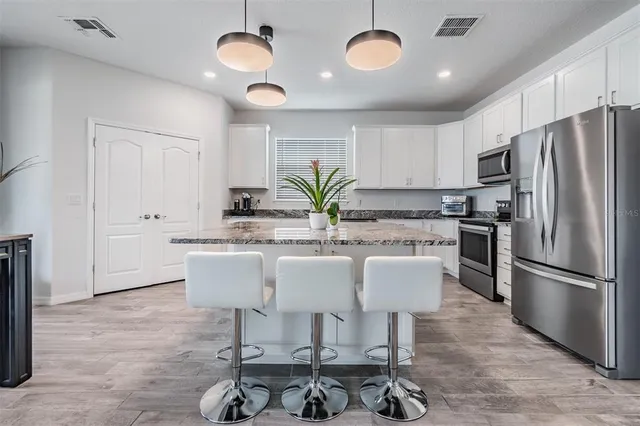 a kitchen with stainless steel appliances granite countertop a stove a sink dishwasher a refrigerator and white cabinets with wooden floor