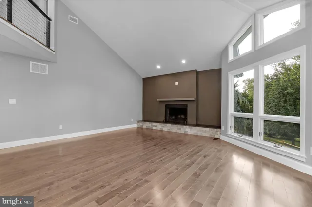 an empty room with wooden floor fireplace and windows