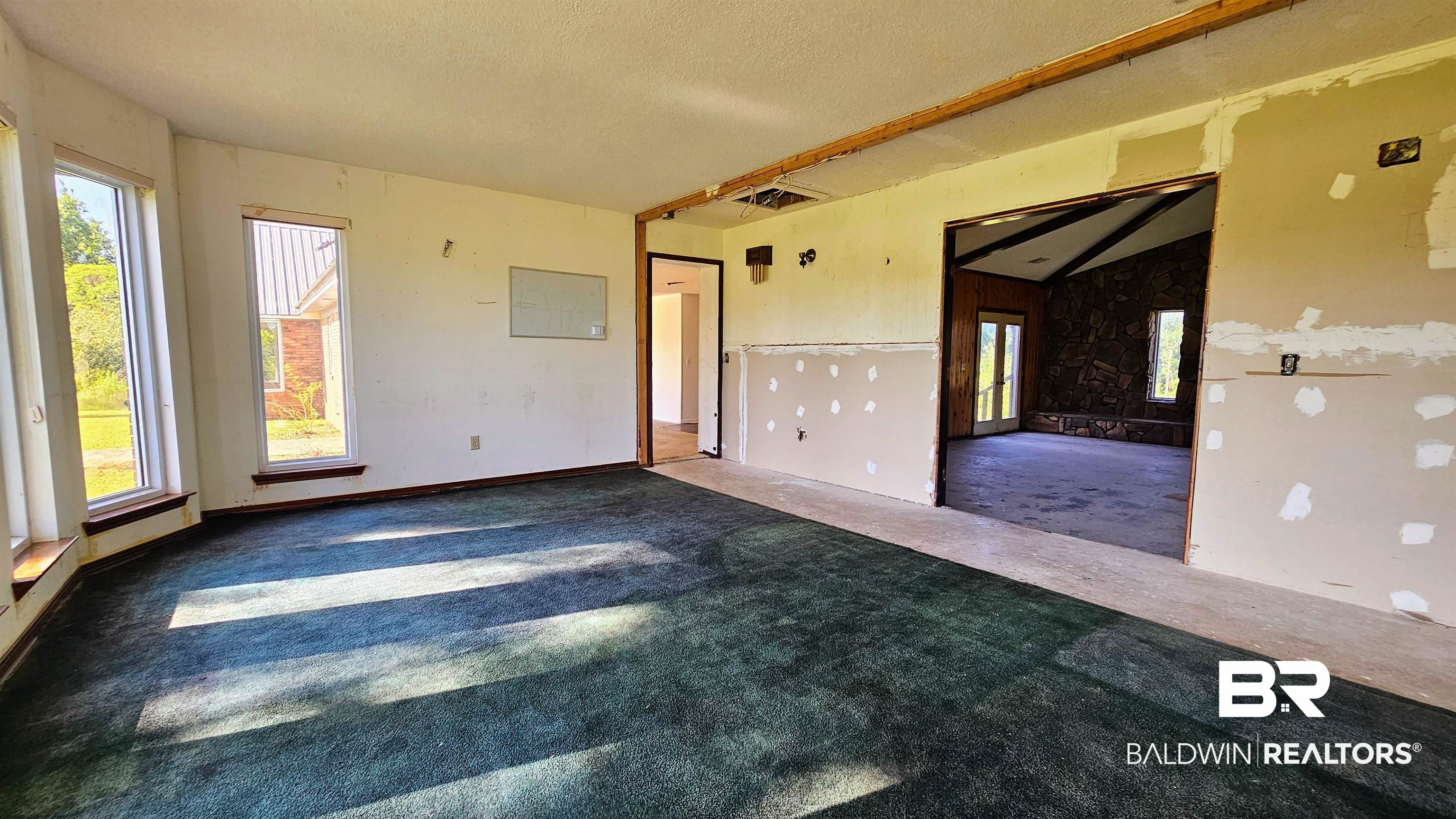 18824 Highway 41 Brewton, AL 36426 - Photo 15 of 40 Interior space with multiple windows, green carpeting, and a doorway leading to a room with exposed ceiling beams and a large window