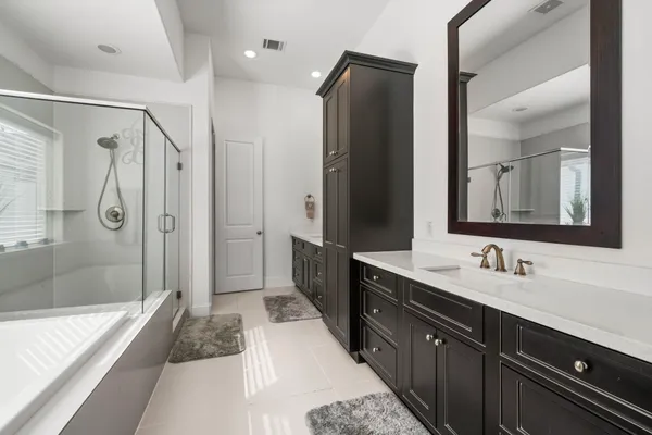 a spacious bathroom with a double vanity sink a large mirror a bathtub and shower