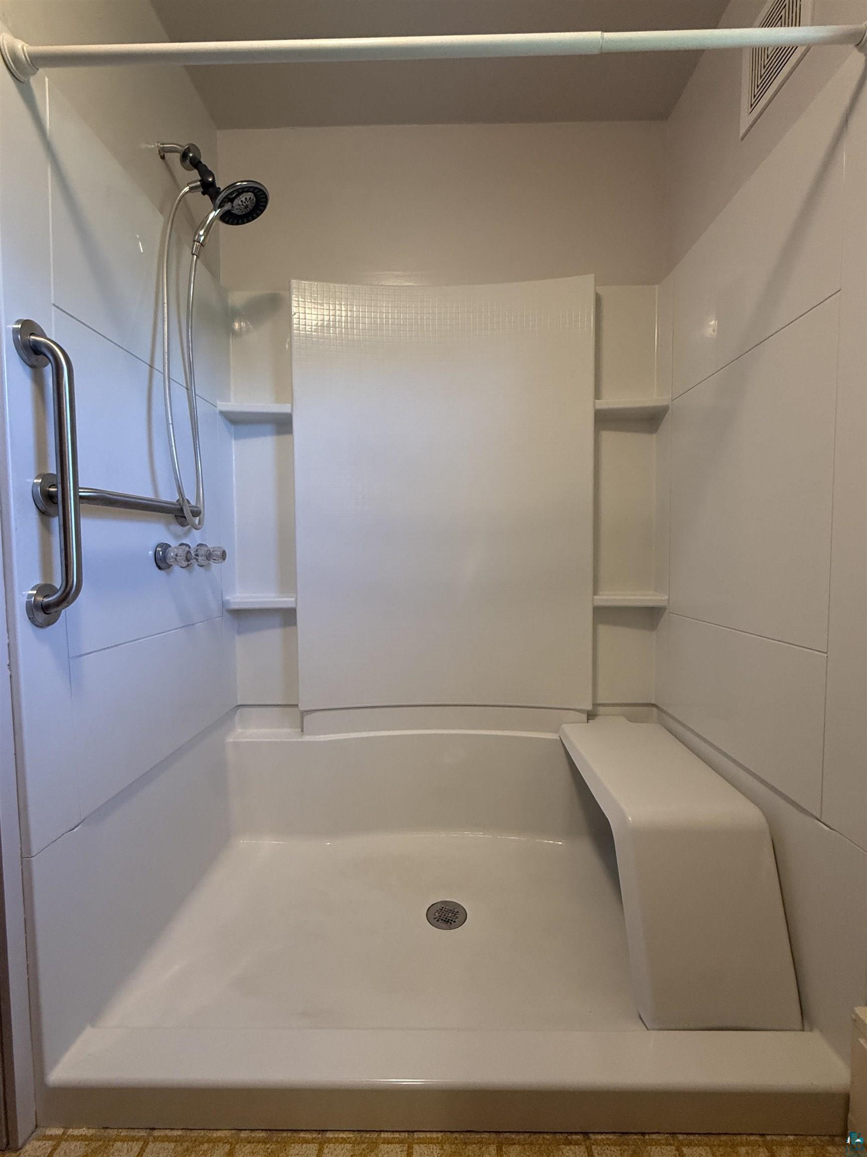 607 3rd Street Northeast Chisholm, MN 55719 - Photo 20 of 32 White shower enclosure featuring a built-in bench, integrated shelving, handheld showerhead, and grab bars