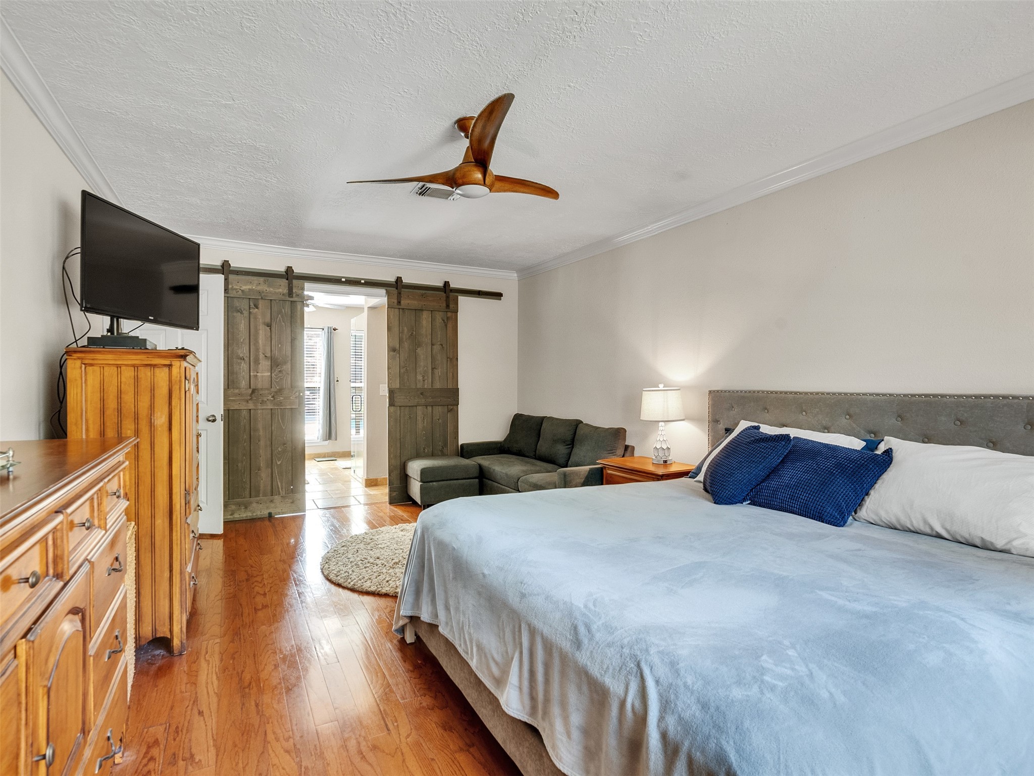 87 South Copper Sage Circle Spring, TX 77381 - Photo 14 of 28 Primary bedroom features warm wood flooring, a cozy seating area, and a stylish ceiling fan. complemented by sliding barn doors leading to the en-suite area, creating a blend of rustic charm and modern comfort.