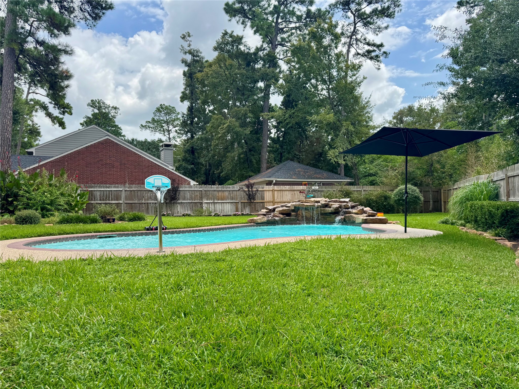 87 South Copper Sage Circle Spring, TX 77381 - Photo 5 of 28 Spacious and Beautiful backyard surrounded by lush greenery A basketball hoop and a large umbrella offer recreational options and shade. Enclosed by a wooden fence, providing privacy for a serene atmosphere.