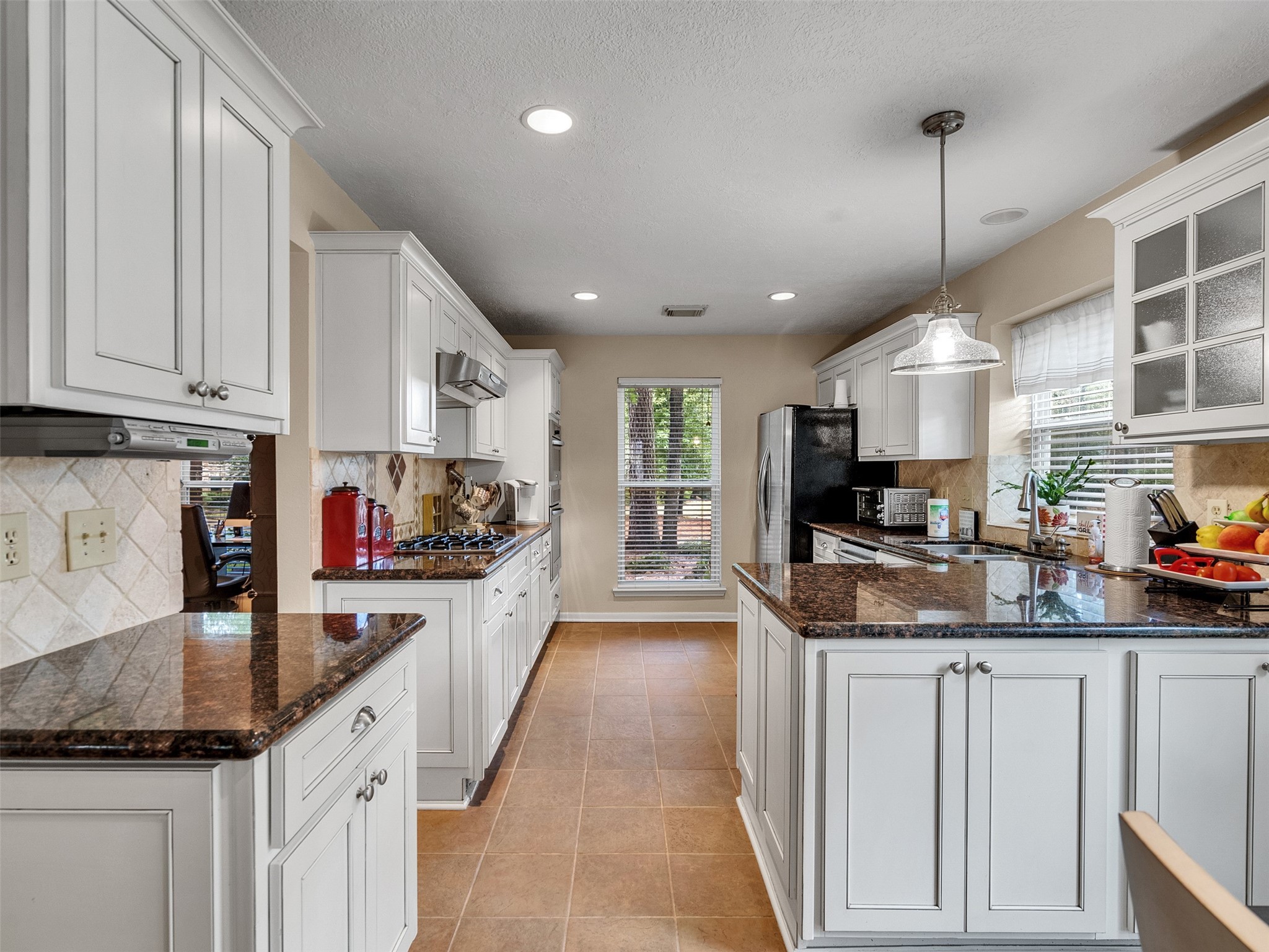 87 South Copper Sage Circle Spring, TX 77381 - Photo 8 of 28 Beautiful updated kitchen featuring elegant white cabinetry, granite countertops, and stainless steel appliances giving it that modern, inviting atmosphere. Natural light fills the space through two windows, complementing the warm tiled flooring.