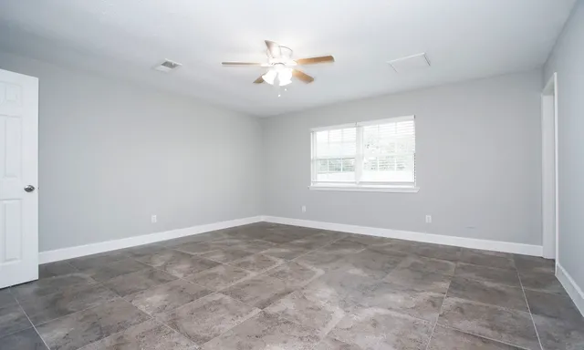 an empty room with chandelier fan and windows