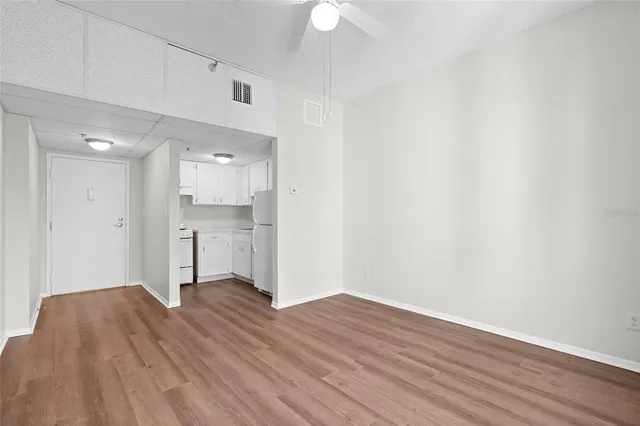 a view of an empty room with wooden floor and a kitchen