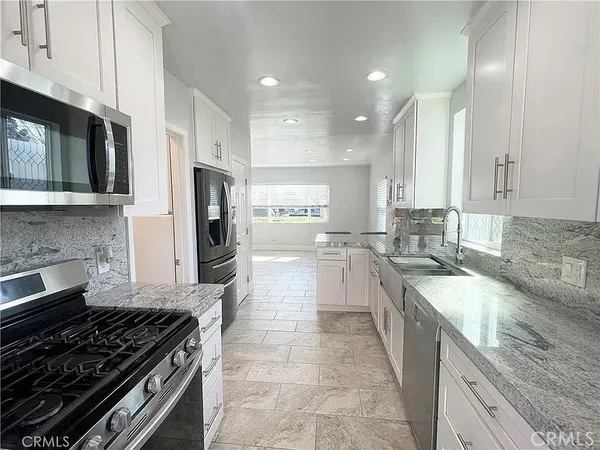 a large kitchen with stainless steel appliances granite countertop a stove top oven a sink dishwasher and a microwave oven with white cabinets