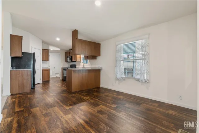 a living room with stainless steel appliances kitchen island granite countertop a stove a refrigerator a sink a microwave oven with wooden floor and cabinets