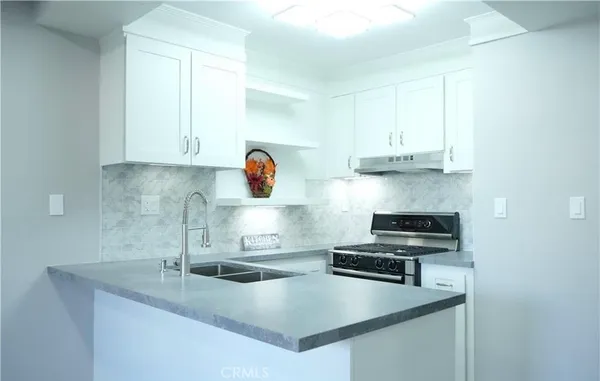 a kitchen with kitchen island granite countertop a sink a stove and white cabinets