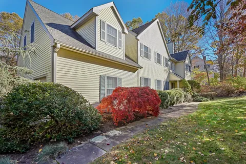 a view of a white house next to a yard with big trees