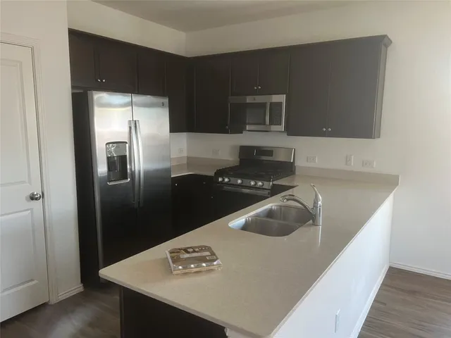 a kitchen with stainless steel appliances granite countertop a refrigerator a sink a stove and wooden floor