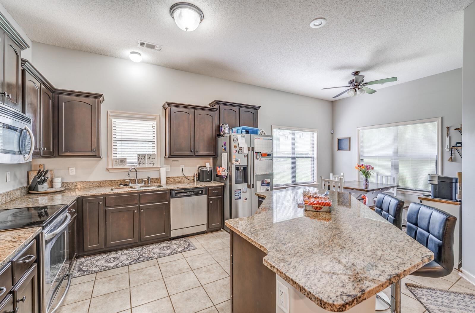 4671 Hampton Ridge Lane Bartlett, TN 38002 - Photo 19 of 40 Kitchen featuring a large island with a stone-finish countertop, dark wood-finish cabinetry, stainless steel appliances, and tile flooring