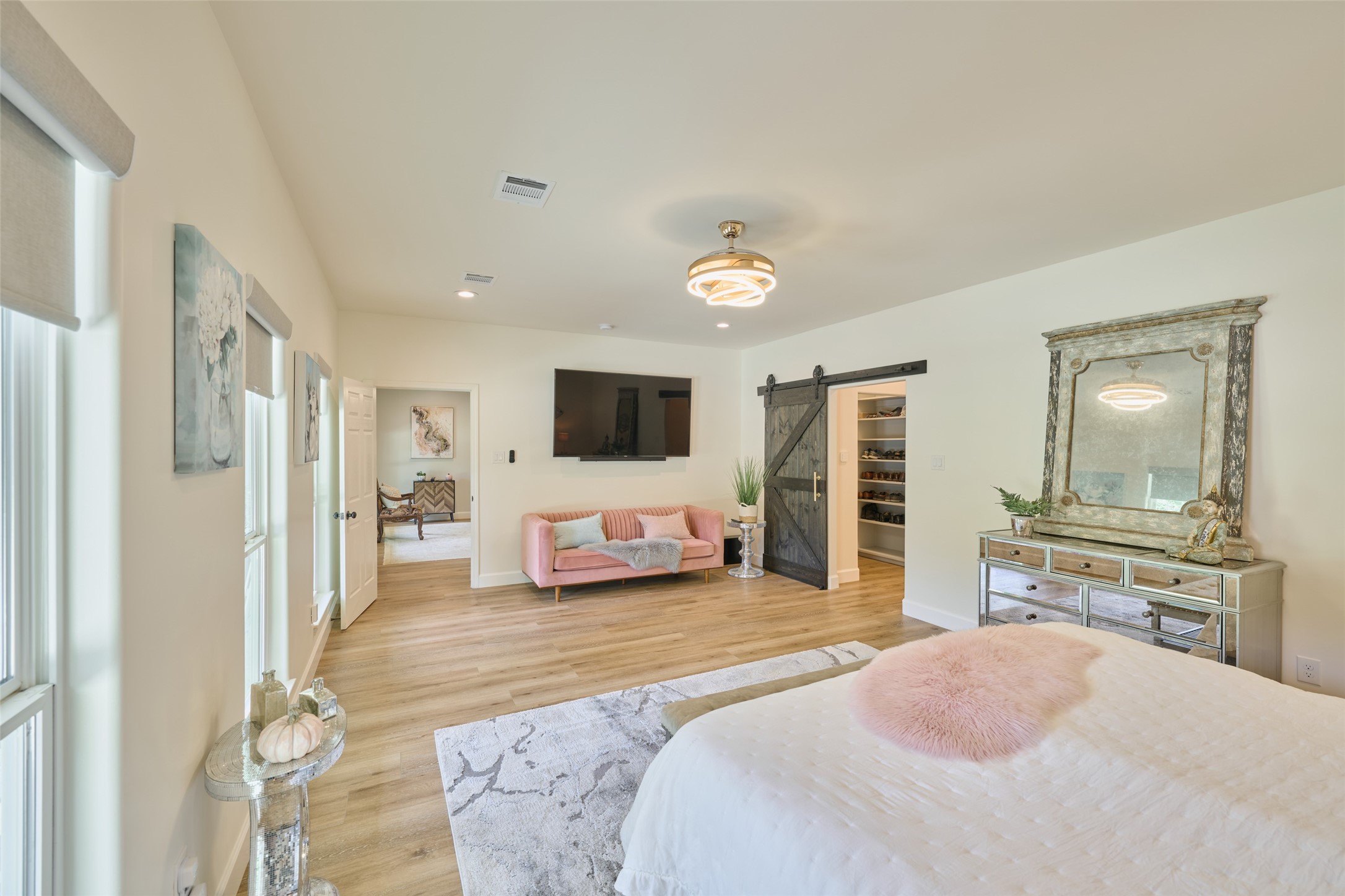 2218 Honea Egypt Road Magnolia, TX 77354 - Photo 29 of 50 This is a spacious, well-lit bedroom featuring hardwood floors, a neutral color palette, modern light fixtures, and a sliding barn door leading to a walk-in closet or ensuite. It's furnished with a large bed, a cozy seating area, and has ample wall space for decor.