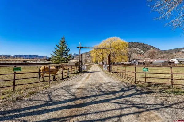 a view of a white house next to a road with large trees
