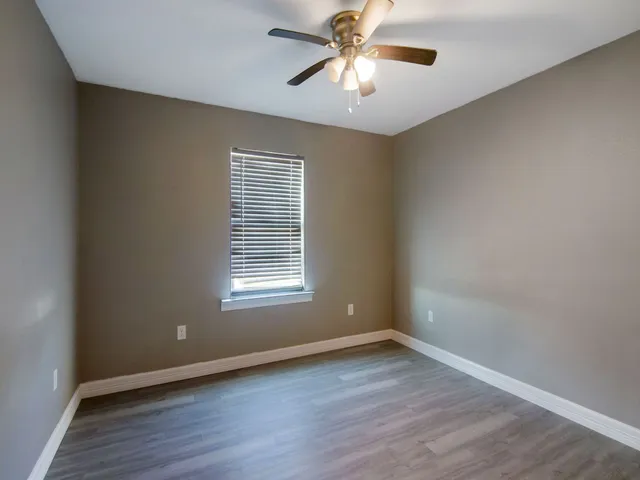 an empty room with wooden floor chandelier fan and windows