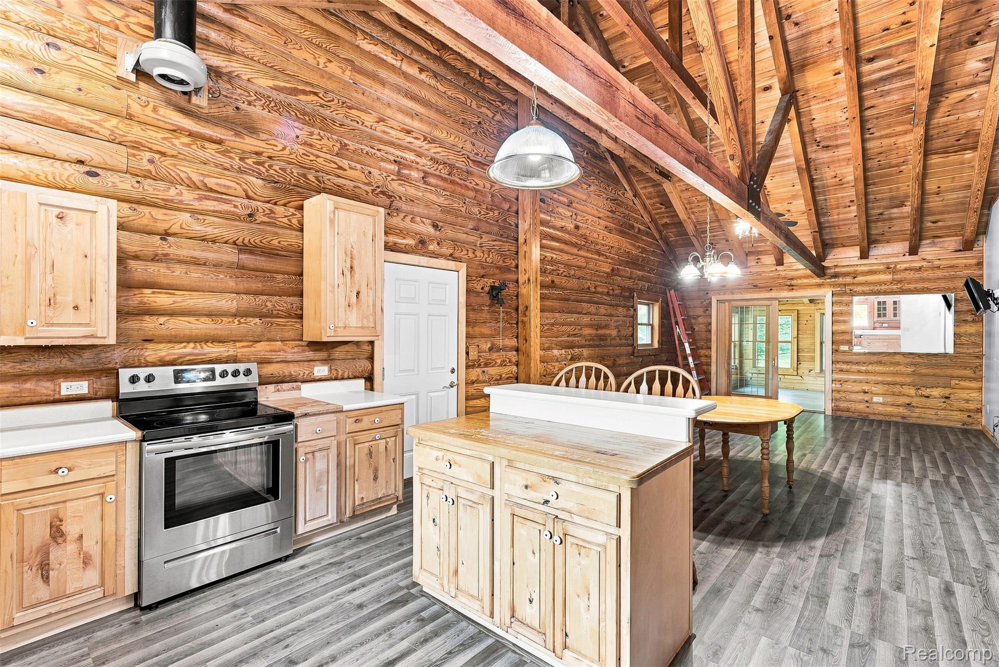 8340 North Nichols Road Flushing, MI 48433 - Photo 34 of 62 Kitchen featuring log walls, wood-finish flooring, stainless steel range, light wood cabinetry, and a center island with a breakfast bar