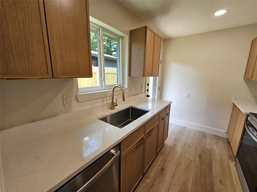 1725 R Avenue, Unit 1725 Plano, TX 75074 - Photo 7 of 20 Modern kitchen featuring wood-finish cabinetry, light-toned countertops, a stainless steel undermount sink, and a gold-tone gooseneck faucet