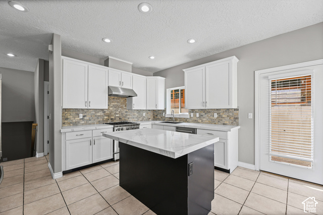 14038 New Saddle Road Draper, UT 84020 - Photo 8 of 46 White shaker cabinetry, stone-look backsplash, stainless steel range with matching hood, central island with stone countertop, and tile flooring