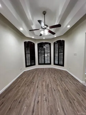 a view of an empty room with chandelier fan and wooden floor