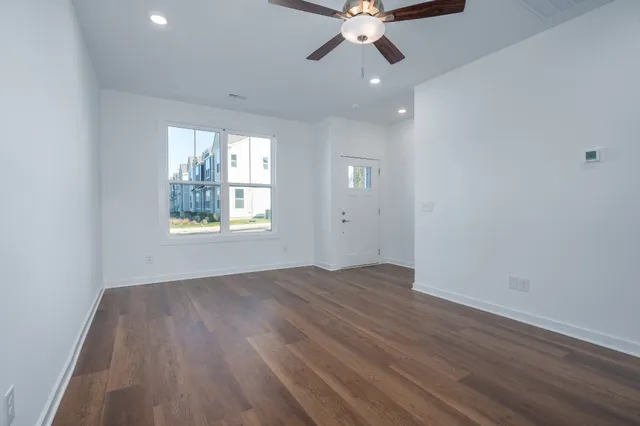 an empty room with wooden floor chandelier fan and windows