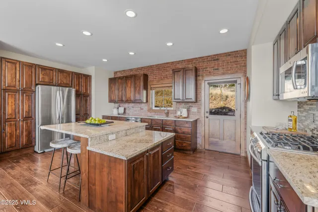 a kitchen with stainless steel appliances granite countertop a stove top oven a sink dishwasher a dining table and chairs with wooden floor