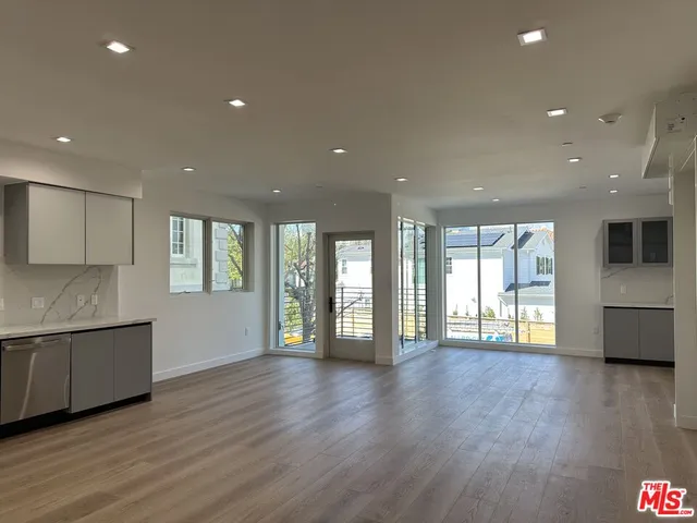 a view of an empty room with wooden floor and a kitchen