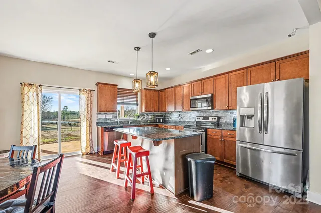 a kitchen with stainless steel appliances granite countertop a refrigerator a stove a sink a dining table and chairs with wooden floor