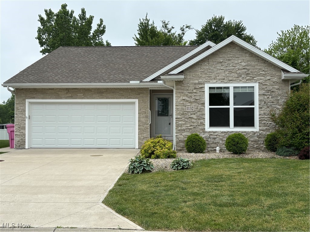 1132 Hummingbird Way Findlay, OH 45840 - Photo 1 of 28 View of front of property featuring stone siding, driveway, a front lawn, an attached garage, and a shingled roof