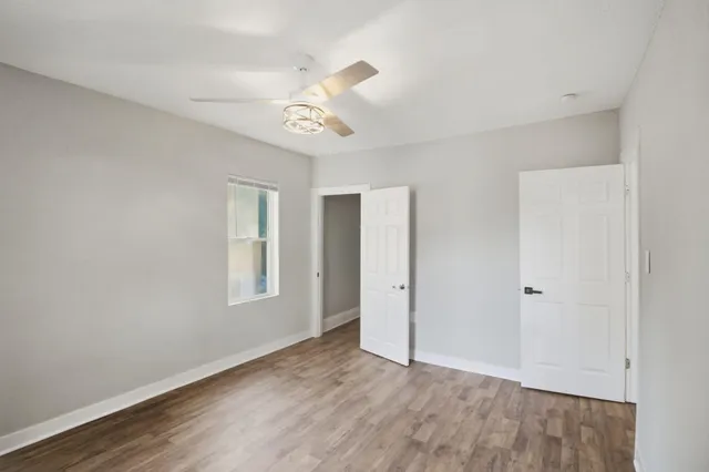 an empty room with wooden floor ceiling fan and windows