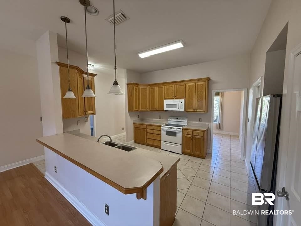10428 South Side Loop Fairhope, AL 36532 - Photo 15 of 28 Kitchen with a peninsula, white appliances, a sink, light countertops, and brown cabinets