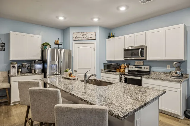 a kitchen with stainless steel appliances granite countertop a sink dishwasher a stove top oven a refrigerator with island and chairs